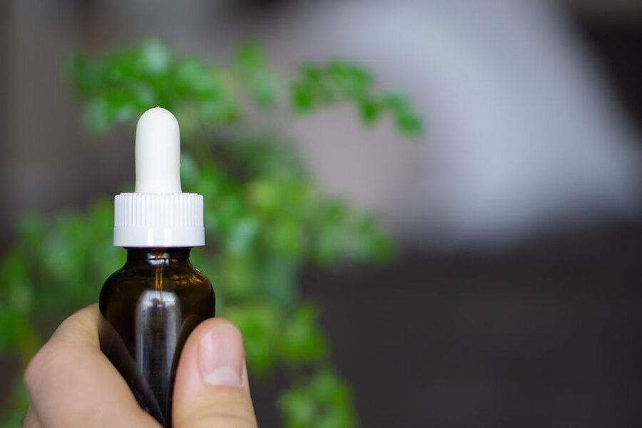 A hand holding a small amber dropper bottle of oil