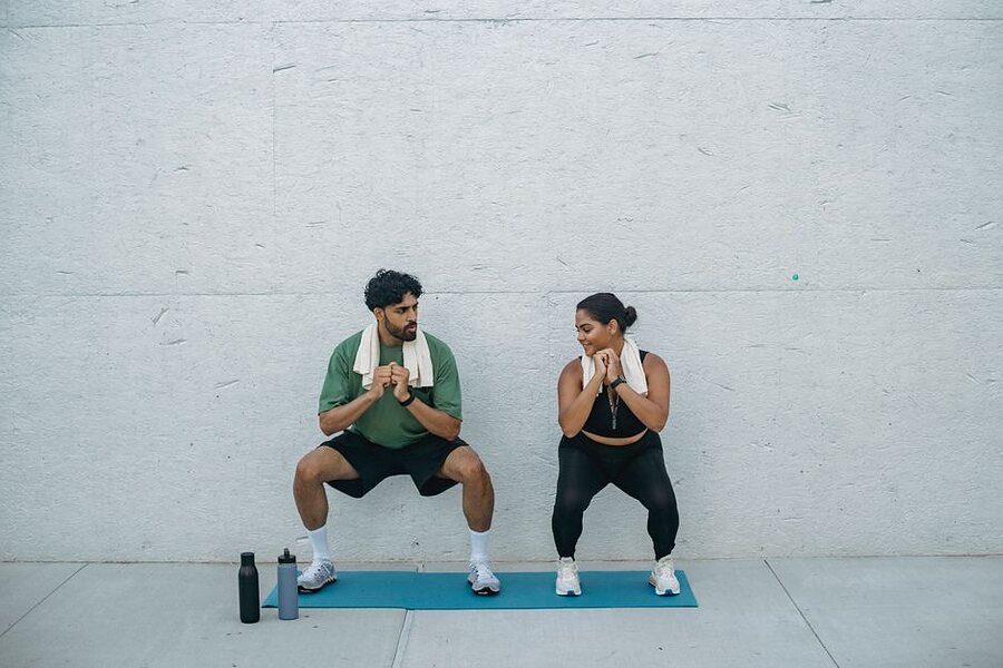 A man and a woman holding a wall sit, backs against a wall, knees bent