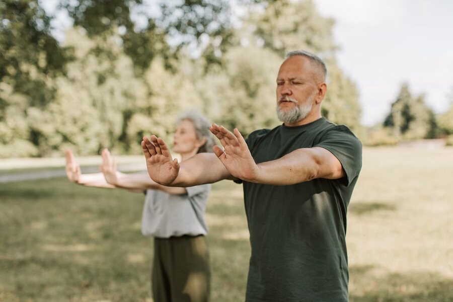 An older couple practising tai chi outdoors in a park