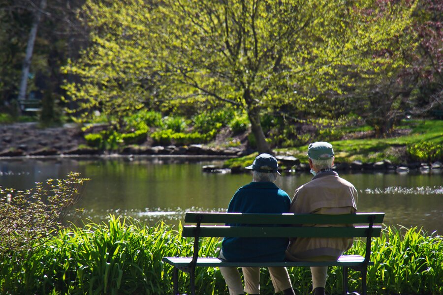Two older people resting on a park bench beside a pond