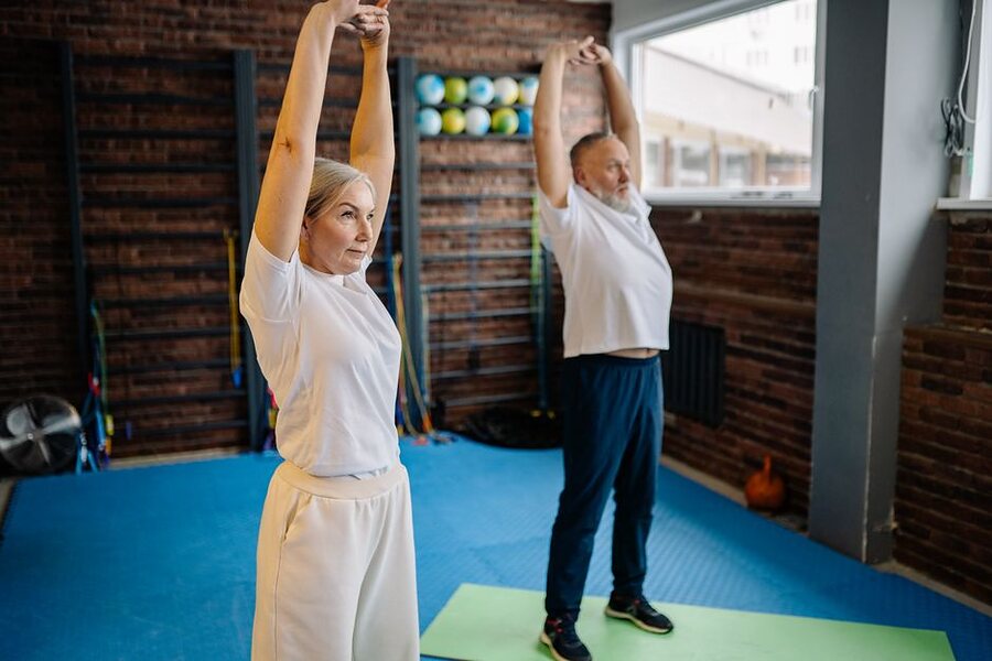 A couple in their fifties doing overhead stretches together