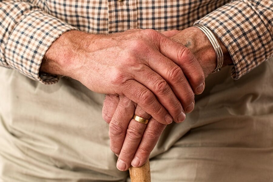 An older man's hands resting on the handle of a walking cane